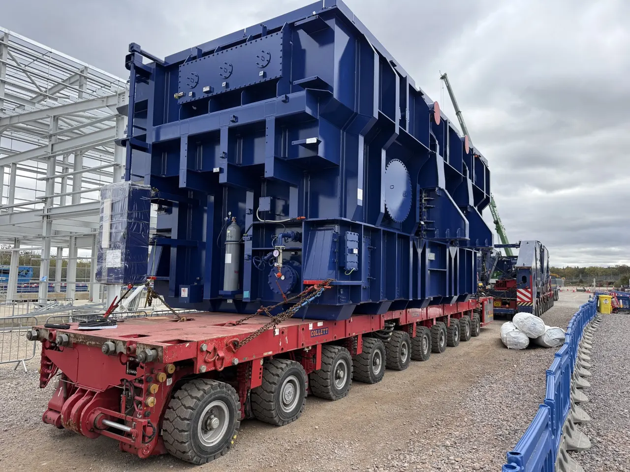 Large super grid transformer positioned on a red self-propelled modular transporter during specialist installation works.
