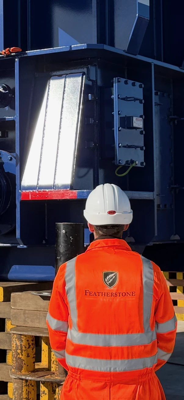 Thomas Featherstone on site in Featherstone Safety coveralls and hard hat, beside a large power transformer.