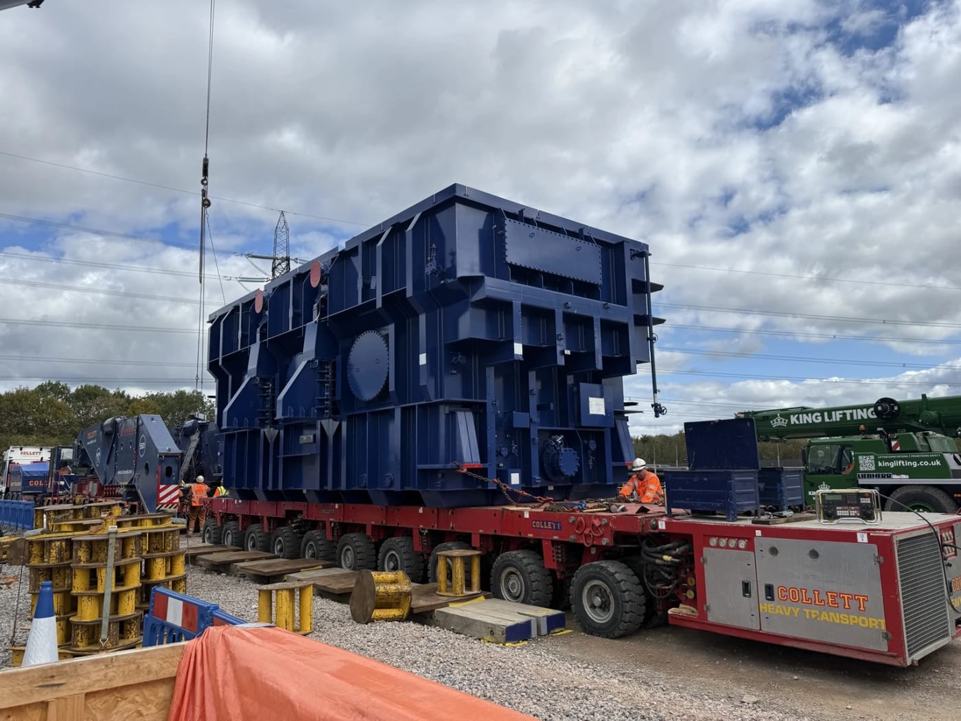 A super grid transformer carried on self propelled modular transporters with a mobile crane alongside.